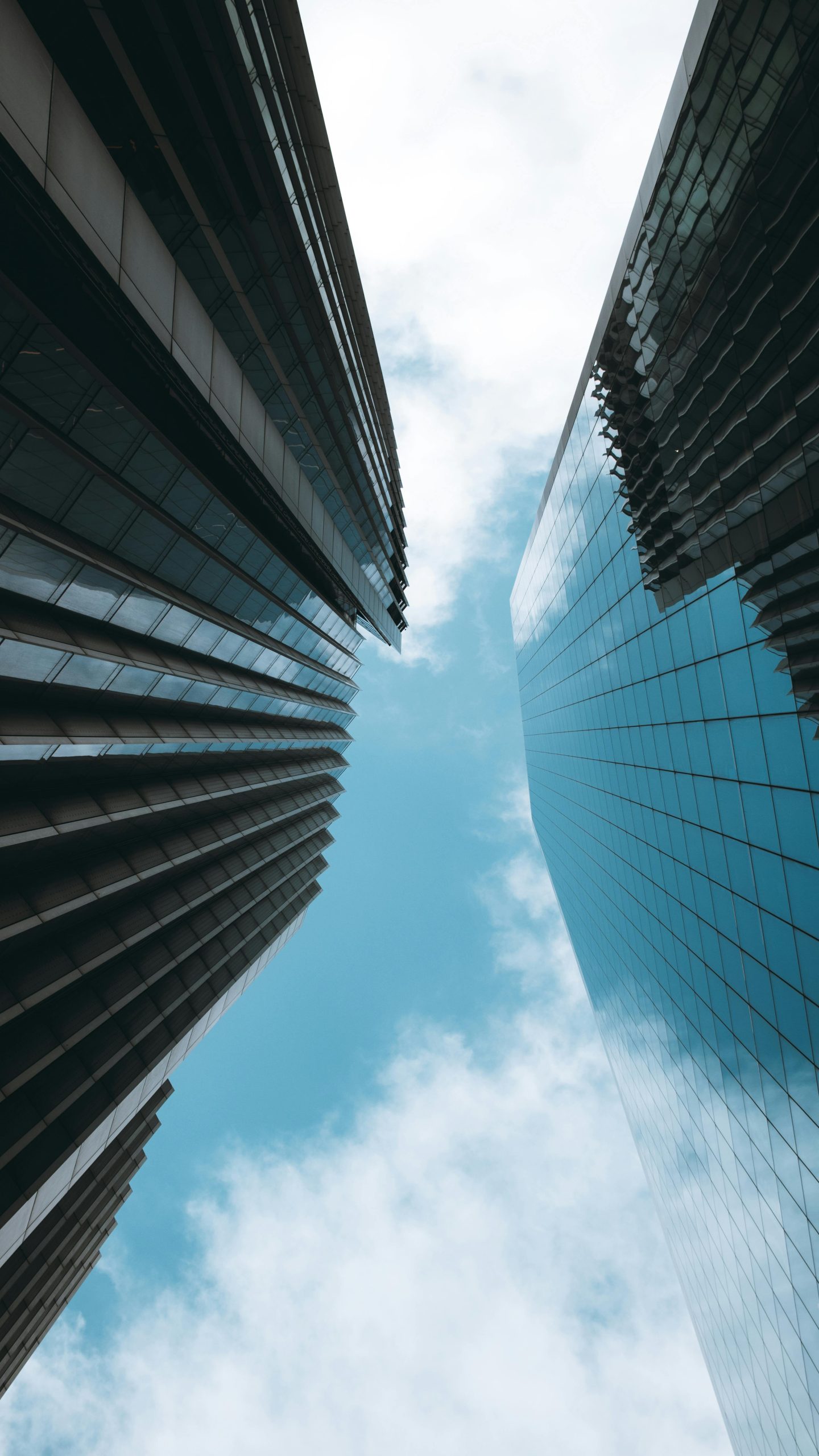 Looking up between two glass skyscrapers toward a blue sky with clouds